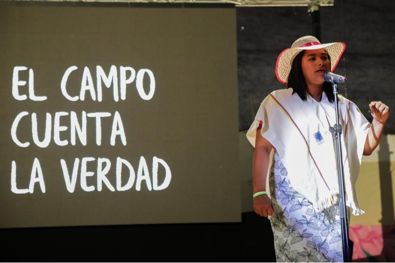 En la imagen una campesina frente a un micrófono con un letrero proyectado que dice: El Campo cuenta la verdad